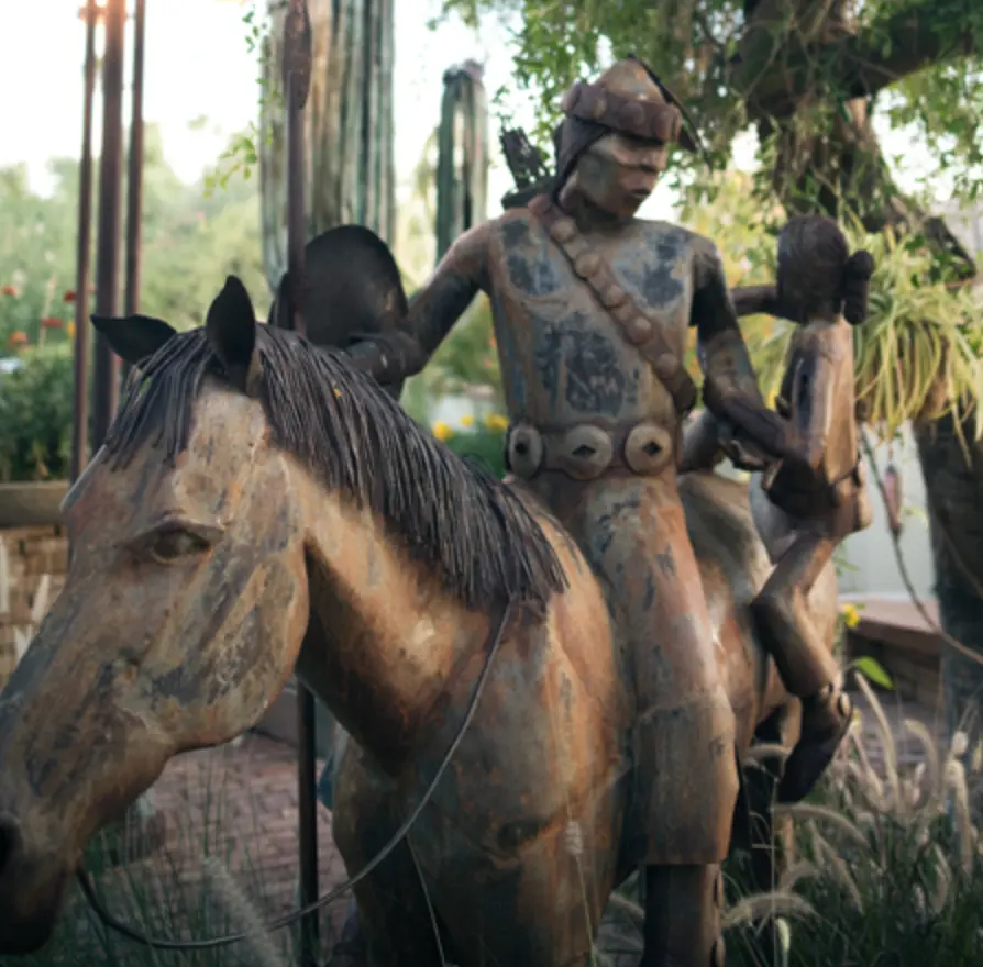 Statue of a decorated indigenous man on a horse while lifting a female child onto the horse.